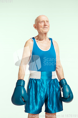 Image of Senior man wearing sportwear boxing on sky background. Concept of sport, activity, movement, wellbeing. Copyspace, ad.