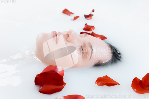 Image of Close up female face in the milk bath with soft white glowing and rose petals. Copyspace for advertising. Beauty, fashion, style, bodycare concept.