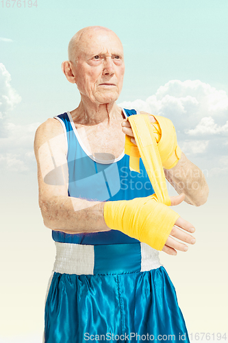 Image of Senior man putting on sportwear for boxing on sky background. Concept of sport, activity, movement, wellbeing. Copyspace, ad.