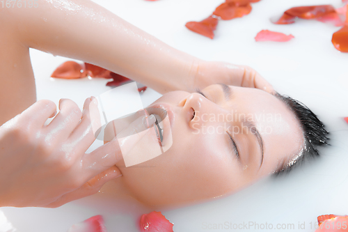 Image of Close up female face in the milk bath with soft white glowing and rose petals. Copyspace for advertising. Beauty, fashion, style, bodycare concept.