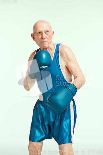 Image of Senior man wearing sportwear boxing isolated on studio background. Concept of sport, activity, movement, wellbeing. Copyspace, ad.