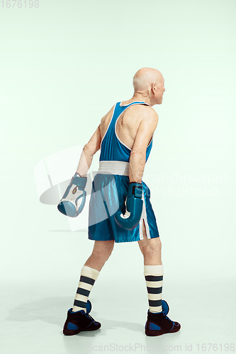 Image of Senior man wearing sportwear boxing isolated on studio background. Concept of sport, activity, movement, wellbeing. Copyspace, ad.