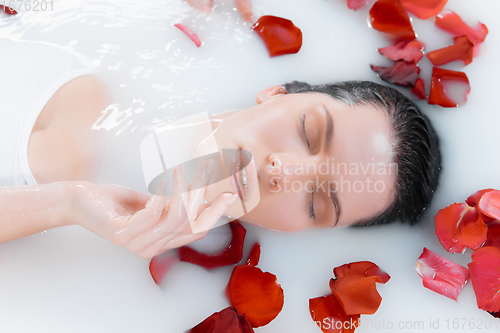 Image of Close up female face in the milk bath with soft white glowing and rose petals. Copyspace for advertising. Beauty, fashion, style, bodycare concept.