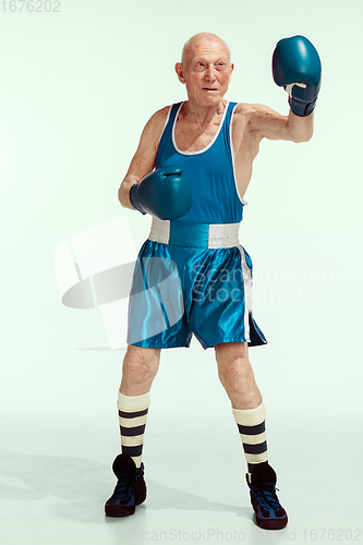 Image of Senior man wearing sportwear boxing isolated on studio background. Concept of sport, activity, movement, wellbeing. Copyspace, ad.