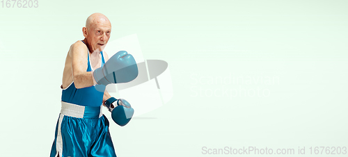 Image of Senior man wearing sportwear boxing isolated on studio background. Concept of sport, activity, movement, wellbeing. Copyspace, ad.