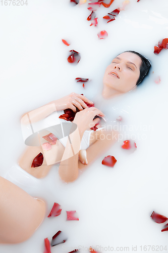 Image of Close up female model in the milk bath with soft white glowing and rose petals. Copyspace for advertising. Beauty, fashion, style, bodycare concept.