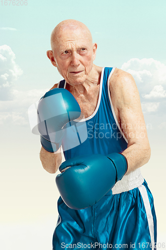 Image of Senior man wearing sportwear boxing on sky background. Concept of sport, activity, movement, wellbeing. Copyspace, ad.