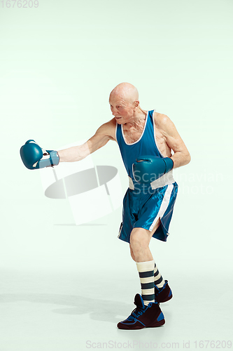 Image of Senior man wearing sportwear boxing isolated on studio background. Concept of sport, activity, movement, wellbeing. Copyspace, ad.