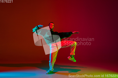 Image of Stylish sportive boy dancing hip-hop in stylish clothes on colorful background at dance hall in neon light. Youth culture, movement, style and fashion, action.