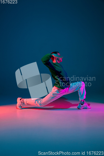 Image of Stylish sportive boy dancing hip-hop in stylish clothes on colorful background at dance hall in neon light. Youth culture, movement, style and fashion, action.