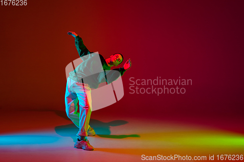 Image of Stylish sportive boy dancing hip-hop in stylish clothes on colorful background at dance hall in neon light. Youth culture, movement, style and fashion, action.