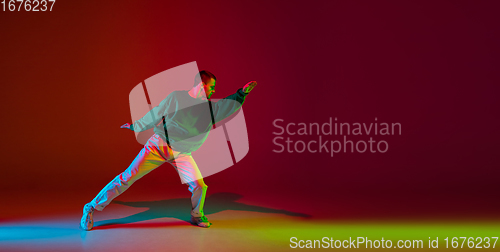 Image of Stylish sportive boy dancing hip-hop in stylish clothes on colorful background at dance hall in neon light. Youth culture, movement, style and fashion, action.