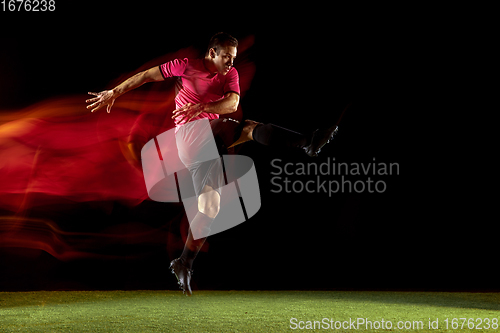 Image of Young football, soccer player of team in action, motion isolated on black background in mixed neon light. Concept of sport, movement, energy and dynamic.
