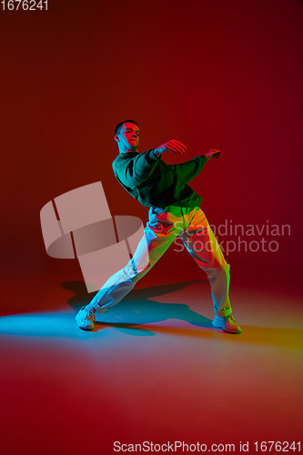 Image of Stylish sportive boy dancing hip-hop in stylish clothes on colorful background at dance hall in neon light. Youth culture, movement, style and fashion, action.