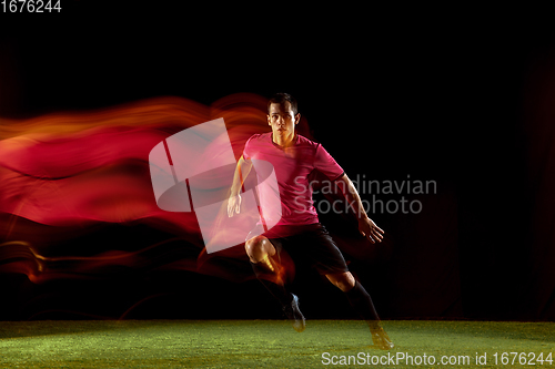 Image of Young football, soccer player of team in action, motion isolated on black background in mixed neon light. Concept of sport, movement, energy and dynamic.