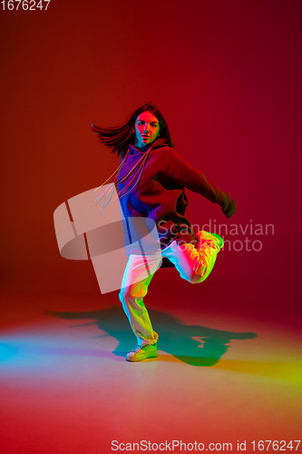 Image of Stylish sportive girl dancing hip-hop in stylish clothes on colorful background at dance hall in neon light. Youth culture, movement, style and fashion, action.