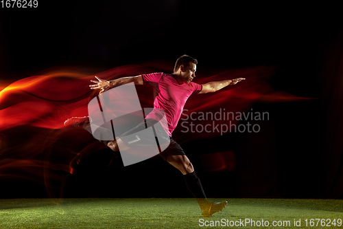 Image of Young football, soccer player of team in action, motion isolated on black background in mixed neon light. Concept of sport, movement, energy and dynamic.