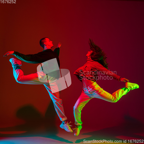 Image of Stylish sportive couple dancing hip-hop in stylish clothes on colorful background at dance hall in neon light. Youth culture, movement, style and fashion, action.