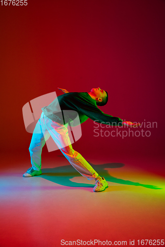 Image of Stylish sportive boy dancing hip-hop in stylish clothes on colorful background at dance hall in neon light. Youth culture, movement, style and fashion, action.
