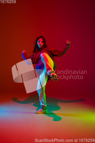 Image of Stylish sportive girl dancing hip-hop in stylish clothes on colorful background at dance hall in neon light. Youth culture, movement, style and fashion, action.