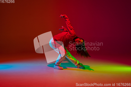 Image of Stylish sportive girl dancing hip-hop in stylish clothes on colorful background at dance hall in neon light. Youth culture, movement, style and fashion, action.