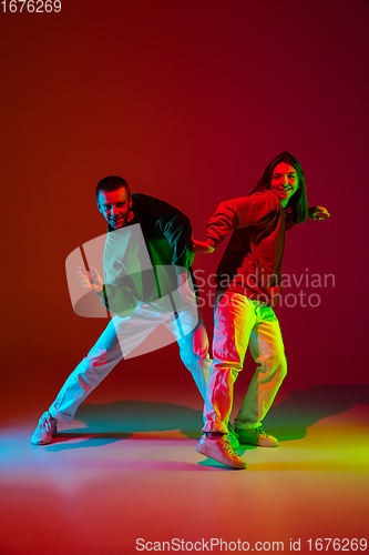 Image of Stylish sportive couple dancing hip-hop in stylish clothes on colorful background at dance hall in neon light. Youth culture, movement, style and fashion, action.