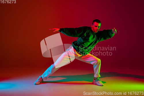 Image of Stylish sportive boy dancing hip-hop in stylish clothes on colorful background at dance hall in neon light. Youth culture, movement, style and fashion, action.