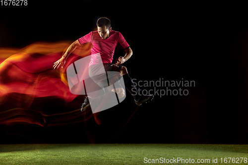 Image of Young football, soccer player of team in action, motion isolated on black background in mixed neon light. Concept of sport, movement, energy and dynamic.