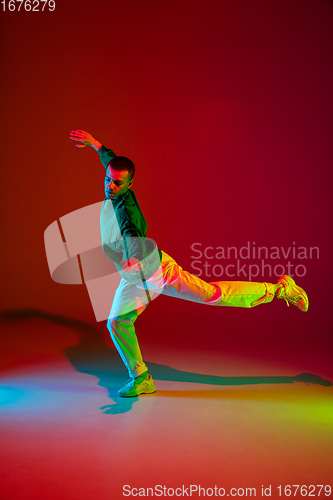 Image of Stylish sportive boy dancing hip-hop in stylish clothes on colorful background at dance hall in neon light. Youth culture, movement, style and fashion, action.