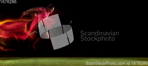 Image of Young football, soccer player of team in action, motion isolated on black background in mixed neon light. Concept of sport, movement, energy and dynamic.