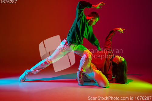 Image of Stylish sportive couple dancing hip-hop in stylish clothes on colorful background at dance hall in neon light. Youth culture, movement, style and fashion, action.