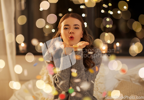 Image of woman blowing confetti from her hands at night