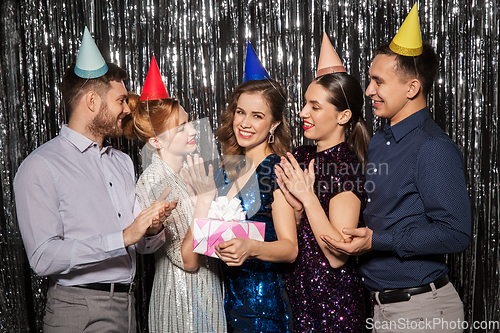 Image of happy friends in party hats with birthday gift