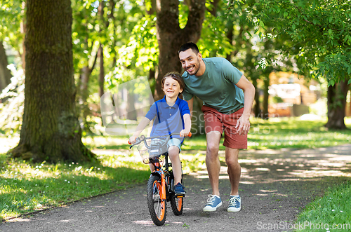 Image of father teaching little son to ride bicycle at park