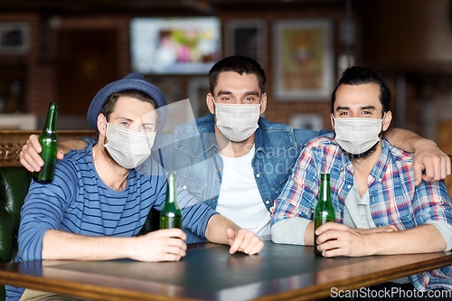 Image of male friends in masks drinking beer at bar or pub