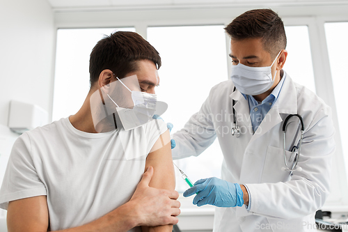 Image of male doctor in mask giving vaccine to patient