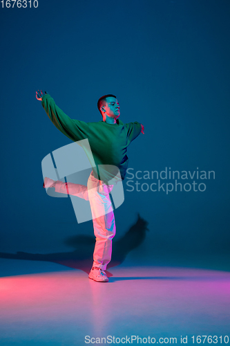 Image of Stylish sportive boy dancing hip-hop in stylish clothes on colorful background at dance hall in neon light. Youth culture, movement, style and fashion, action.