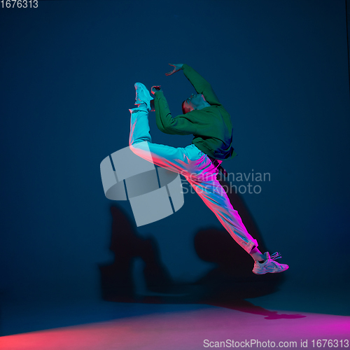 Image of Stylish sportive boy dancing hip-hop in stylish clothes on colorful background at dance hall in neon light. Youth culture, movement, style and fashion, action.