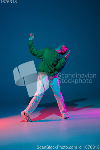 Image of Stylish sportive boy dancing hip-hop in stylish clothes on colorful background at dance hall in neon light. Youth culture, movement, style and fashion, action.