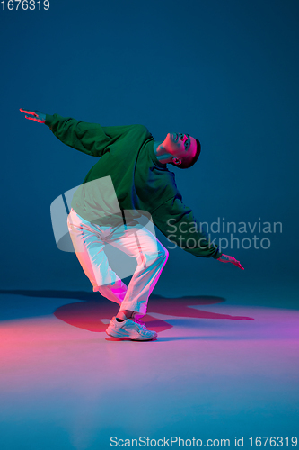 Image of Stylish sportive boy dancing hip-hop in stylish clothes on colorful background at dance hall in neon light. Youth culture, movement, style and fashion, action.