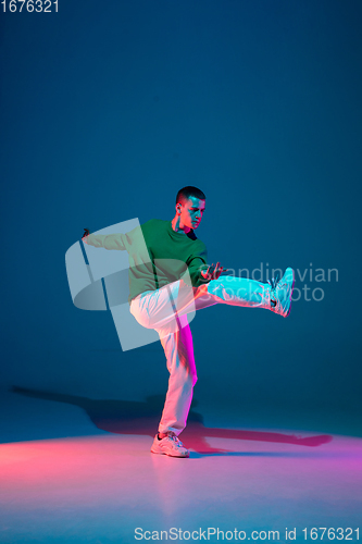 Image of Stylish sportive boy dancing hip-hop in stylish clothes on colorful background at dance hall in neon light. Youth culture, movement, style and fashion, action.