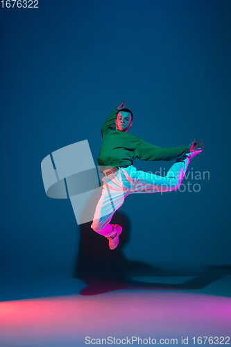 Image of Stylish sportive boy dancing hip-hop in stylish clothes on colorful background at dance hall in neon light. Youth culture, movement, style and fashion, action.