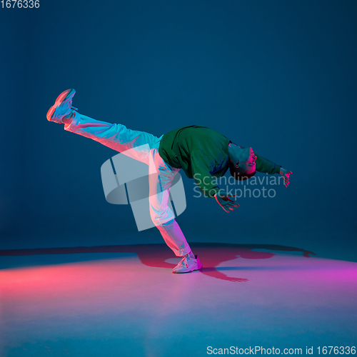 Image of Stylish sportive boy dancing hip-hop in stylish clothes on colorful background at dance hall in neon light. Youth culture, movement, style and fashion, action.