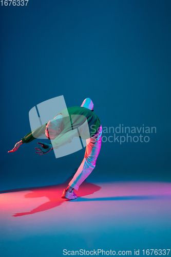 Image of Stylish sportive boy dancing hip-hop in stylish clothes on colorful background at dance hall in neon light. Youth culture, movement, style and fashion, action.