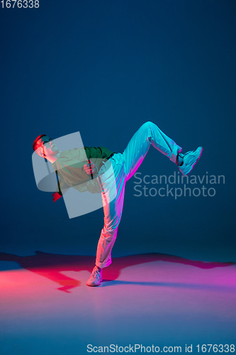 Image of Stylish sportive boy dancing hip-hop in stylish clothes on colorful background at dance hall in neon light. Youth culture, movement, style and fashion, action.