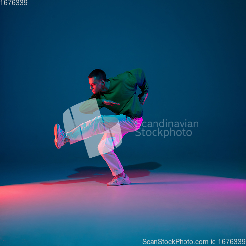 Image of Stylish sportive boy dancing hip-hop in stylish clothes on colorful background at dance hall in neon light. Youth culture, movement, style and fashion, action.