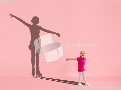 Image of Childhood and dream about big and famous future. Conceptual image with girl and shadow of fit female figure skater on coral pink background