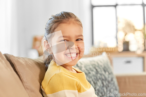 Image of happy smiling little girl sitting on sofa at home
