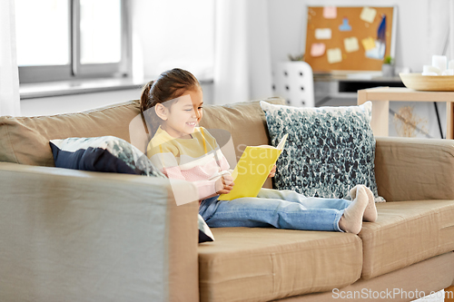 Image of happy smiling little girl reading book at home