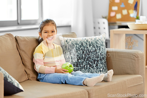 Image of happy little girl with apple sitting on sofa
